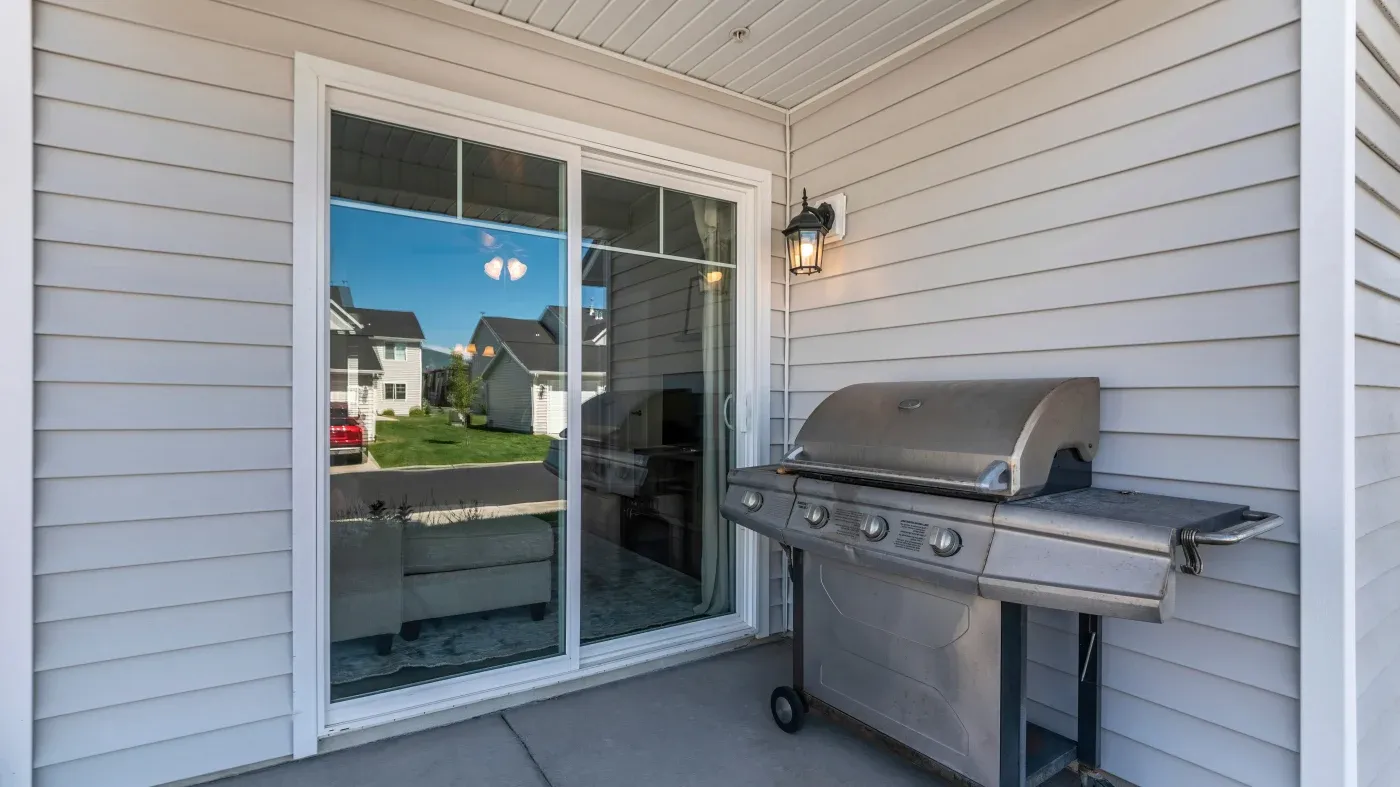 A two-panel sliding patio door with a white frame leads into a home from the deck. There is a grill on the deck.