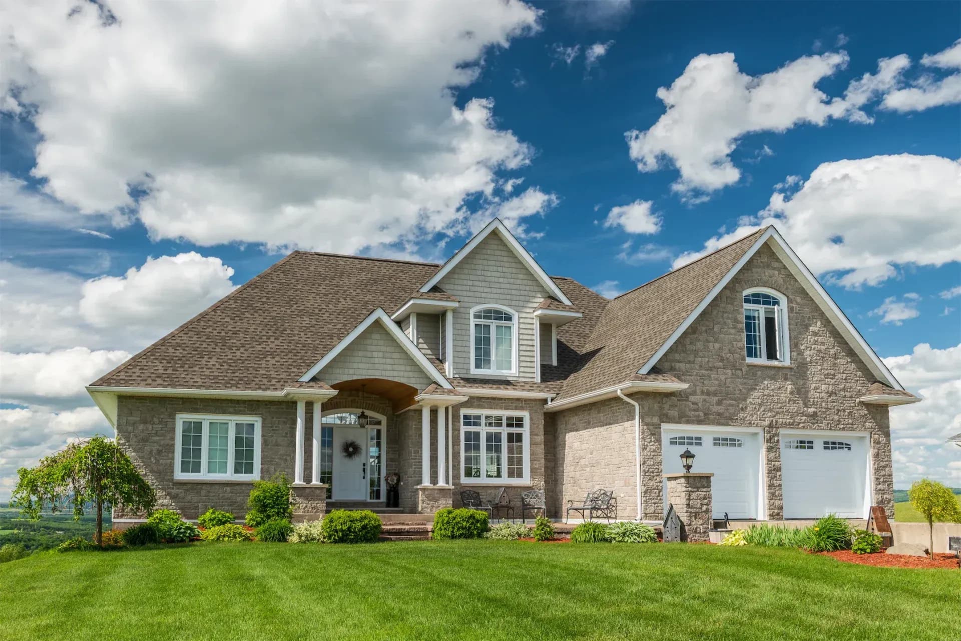 A light-colored stone house with two-car garage and large front lawn.