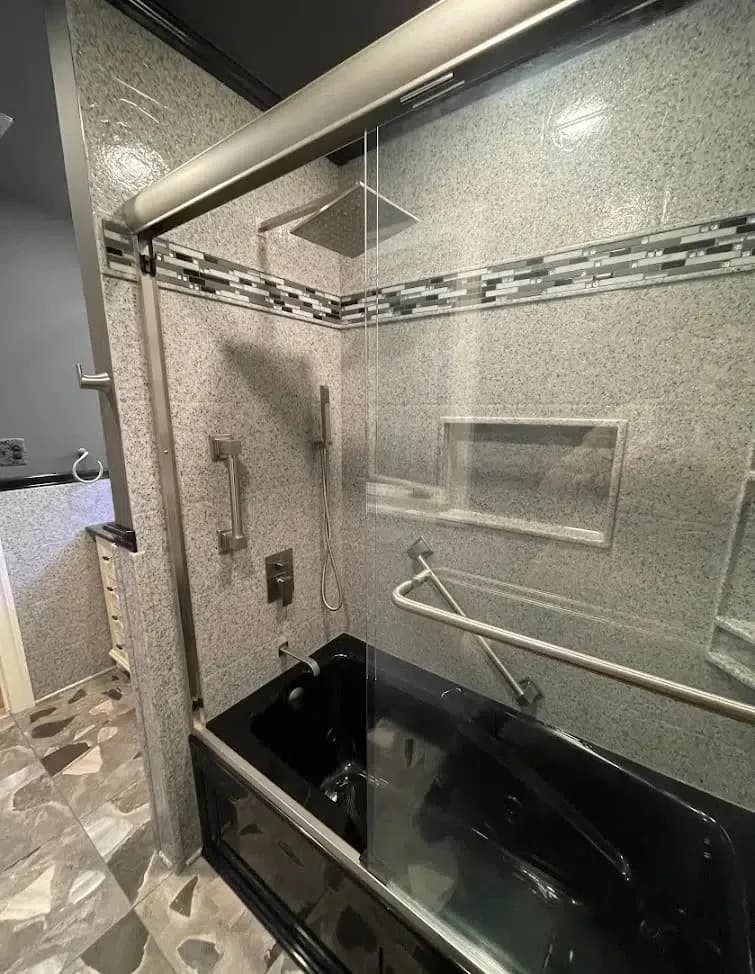 A new black tub with a solid stone surround, two different storage shelves in the walls, two grab bars, new hardware, and a custom tile design.
