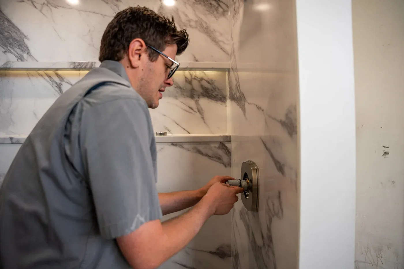 A certified factory-trained walk-in shower installer with Ozark Home Pros in Northwest AR working on hardware in a newly-installed walk-in shower.