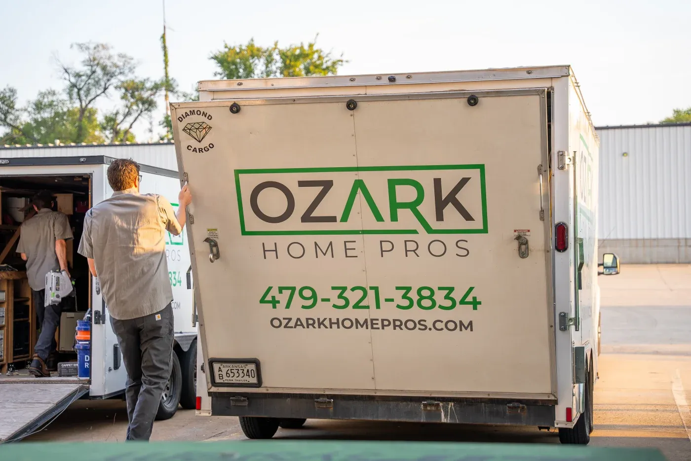 Two team members of Ozark Home Pros loading and unloading different company work trailers in the sunshine.