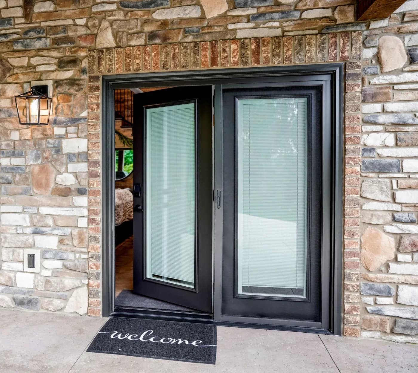 A residential entryway remodeled with a new smooth steel front entry door in rustic bronze with white internal blinds and a welcome mat below.