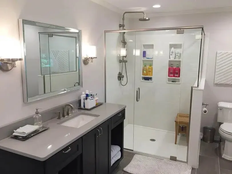 A newly remodeled residential bathroom with new walk-in shower beside the sink area with a wood seat, plenty of custom storage shelves for toiletries, and new chrome hardware.