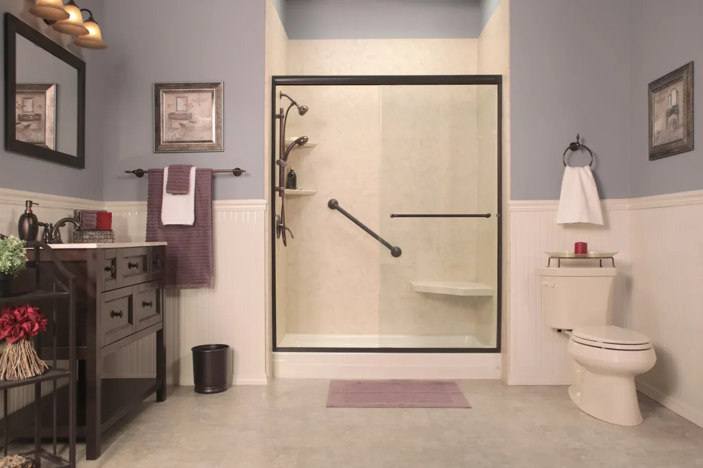 A new walk-in shower in a residential bathroom with rubbed bronze bypass door, grab bar, seating, and new hardware, along with a toilet and small vanity.