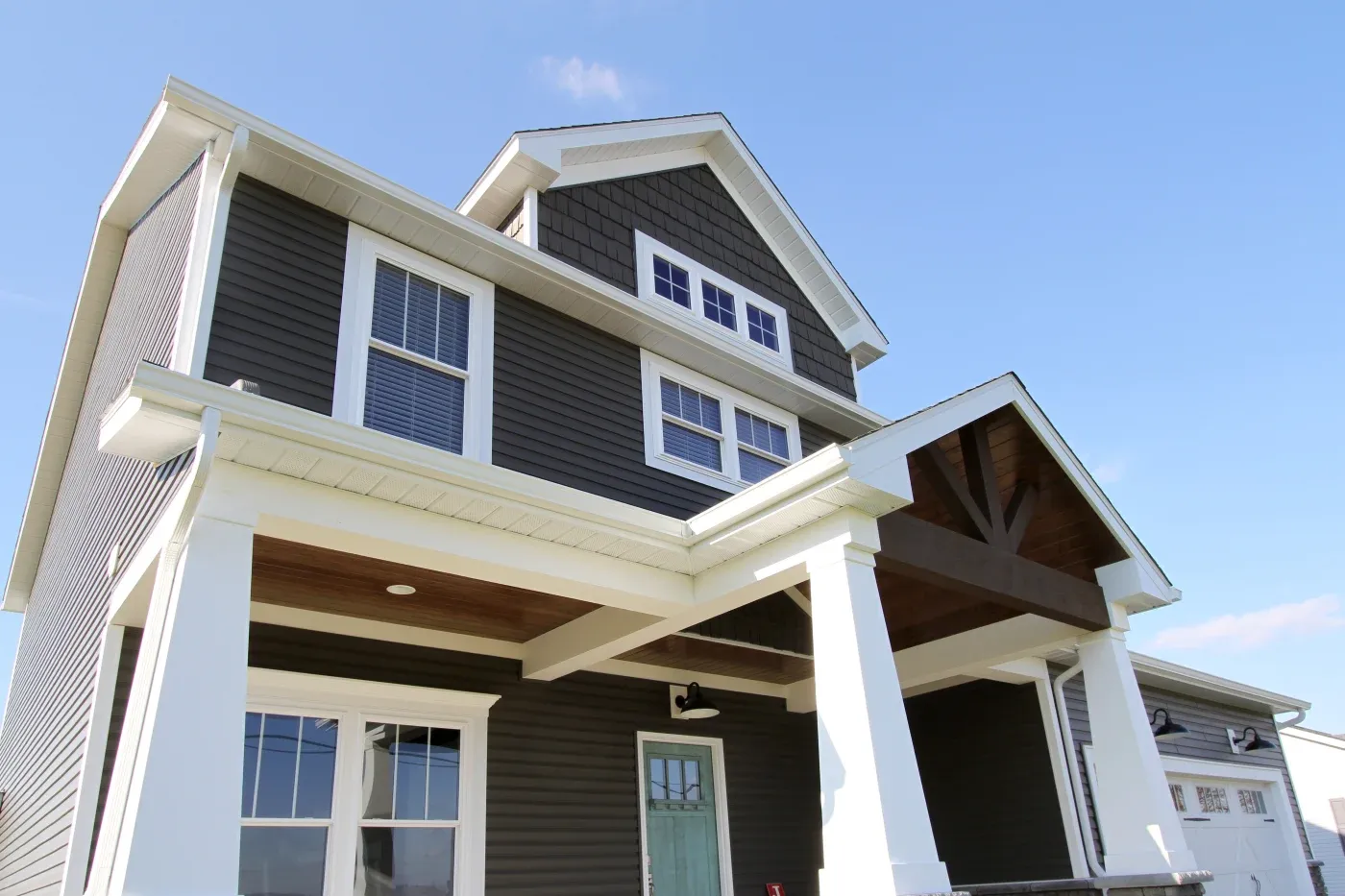 A large two-story residential home with dark brown panel siding, white gutters, white trim, and a variety of new replacement windows – some with internal grids.