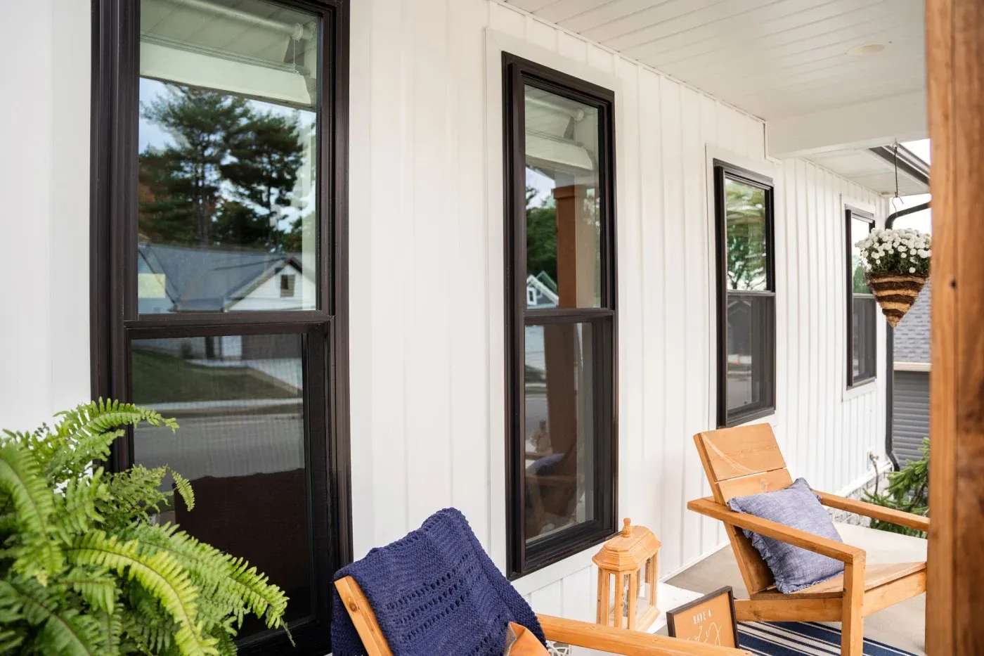 The front porch of a Northwest AR home showing a row of four double-hung replacement windows along with plants in pots and a few lounging chairs.