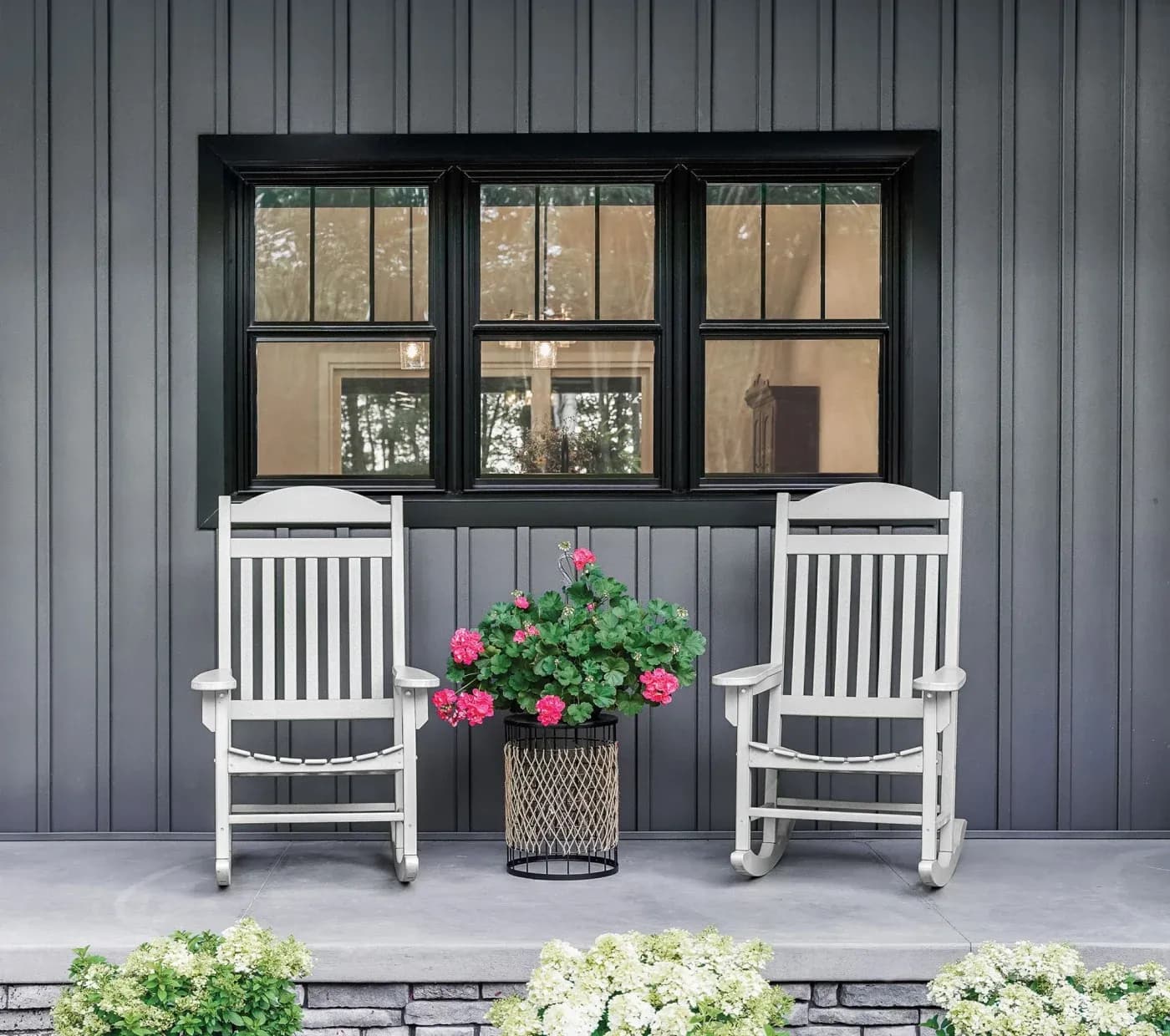 A portion of a residential porch showing two white rocking chairs and a flower pot in the middle, with a set of three double-hung windows behind them in matte coal black with internal grids.