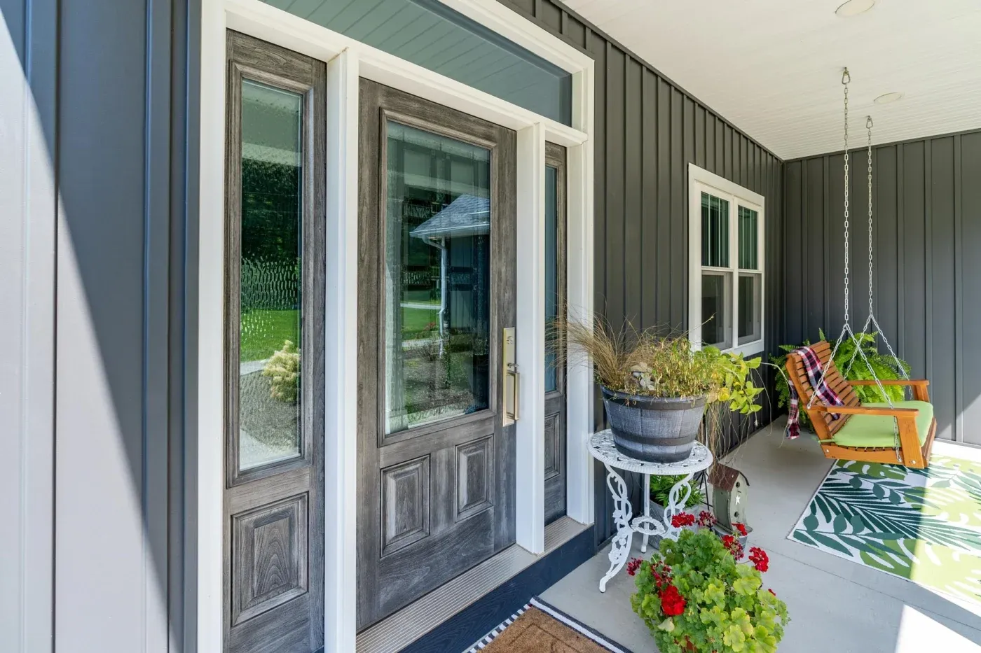 A side view of a residential porch in NW Arkansas showing a new entry door in Dutch gray with Laurance decorative glass, side lites, and golden hardware.
