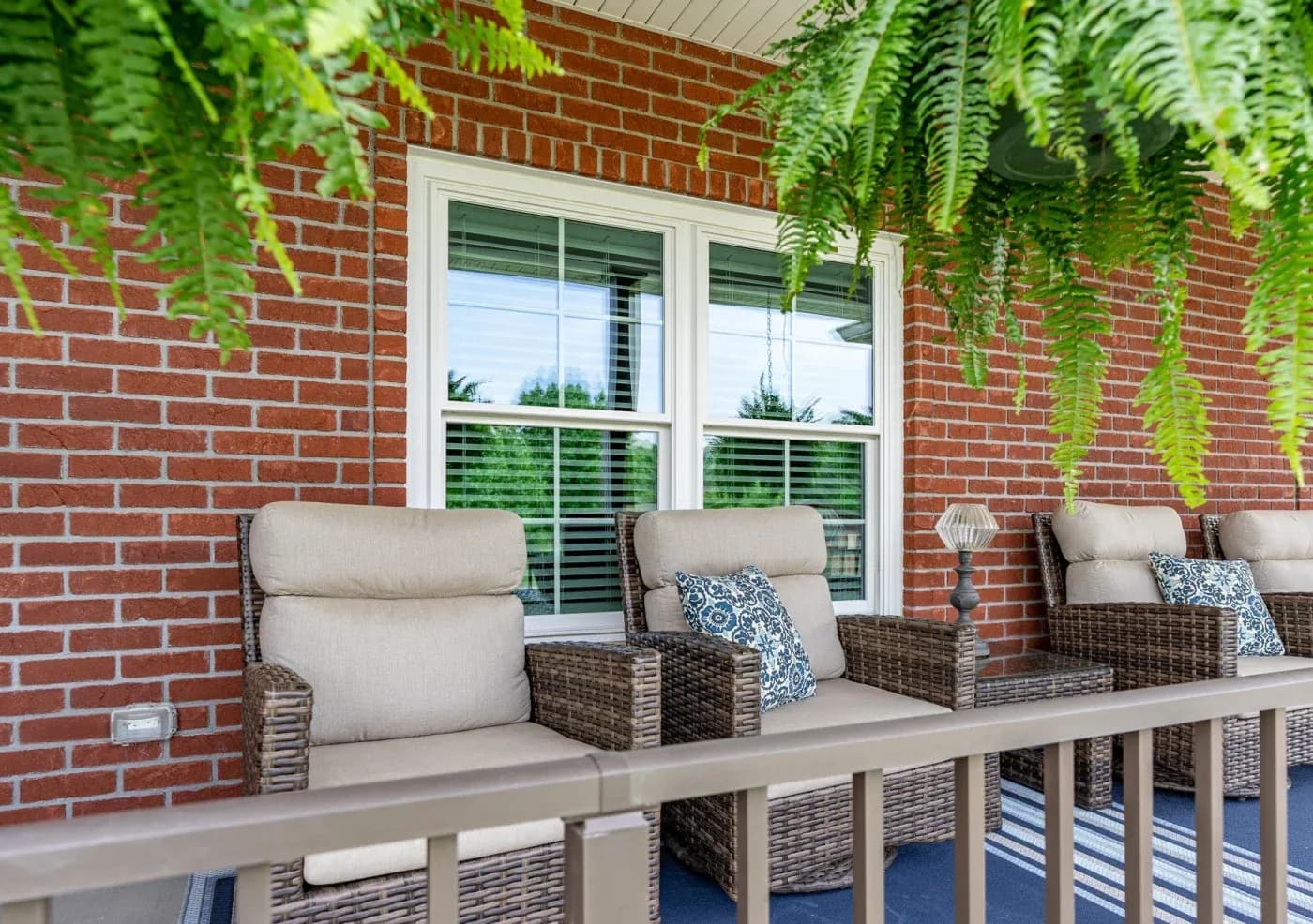 The front of a home looking at a section of the patio with two double-hung windows with cottage grids in white in contrast to the brick siding.