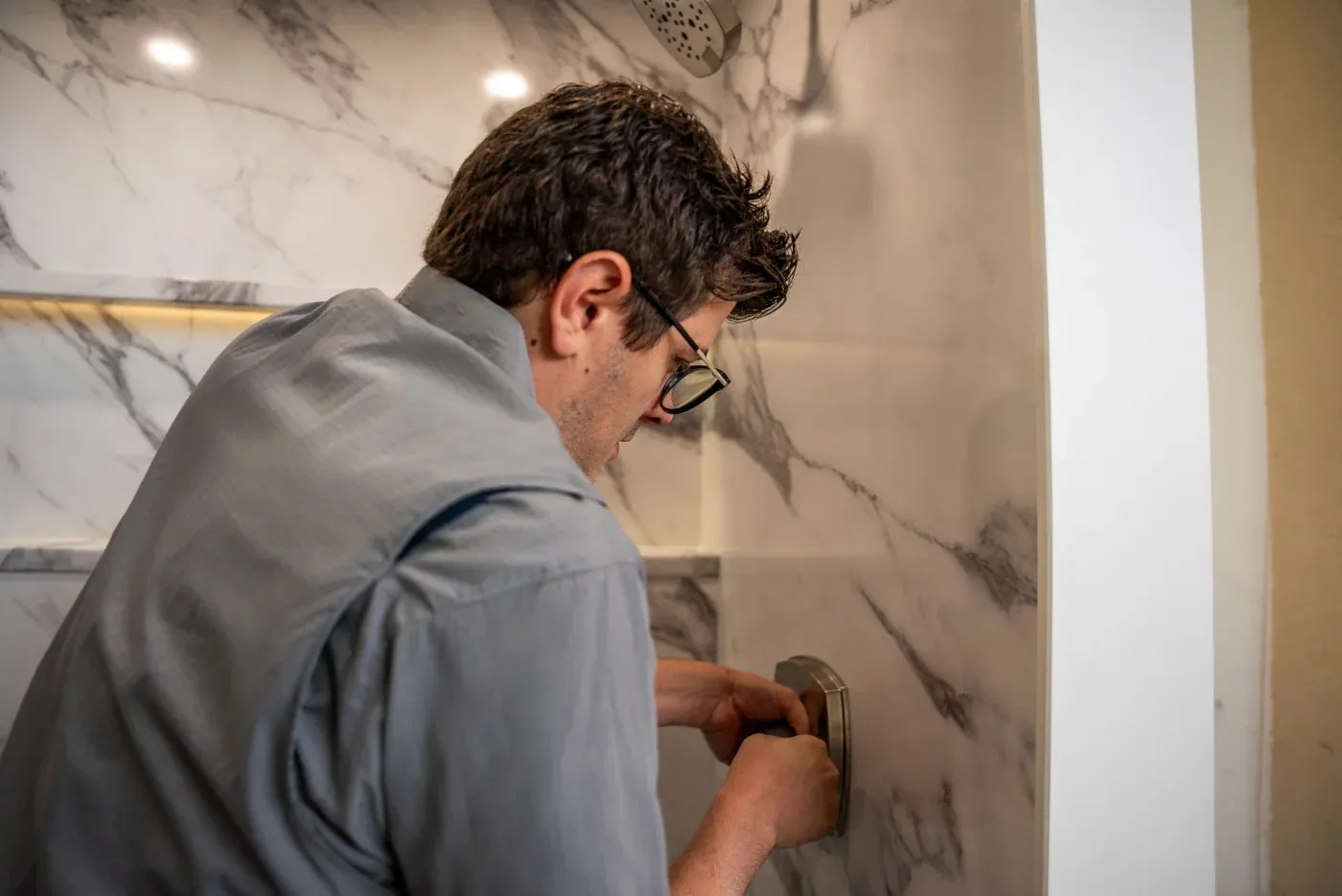 An Ozark Home Pros walk-in shower installer working on the main hardware for a new shower installed in a Northwest Arkansas home.