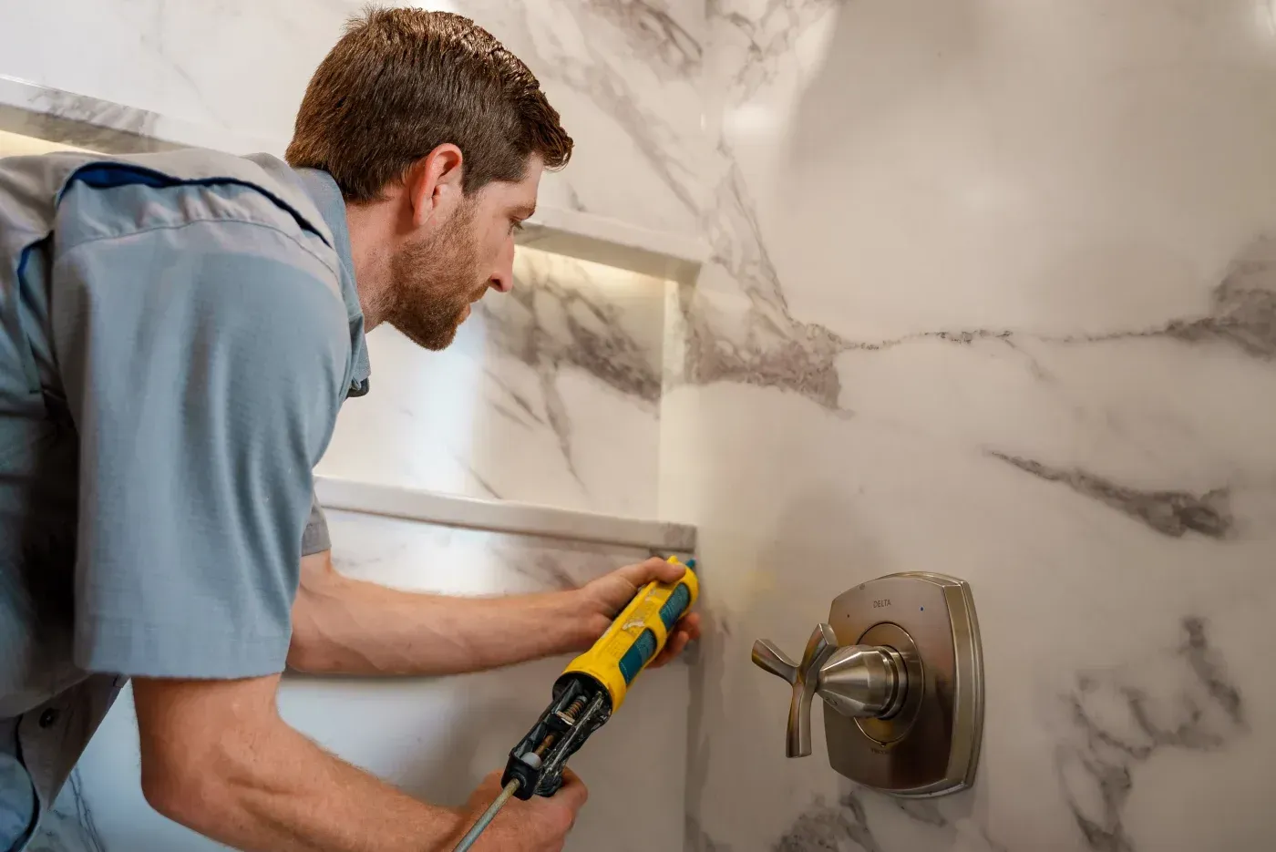 An Ozark Home Pros shower installer applying special caulking in a new tub-to-shower conversion in a Northwest Arkansas home.