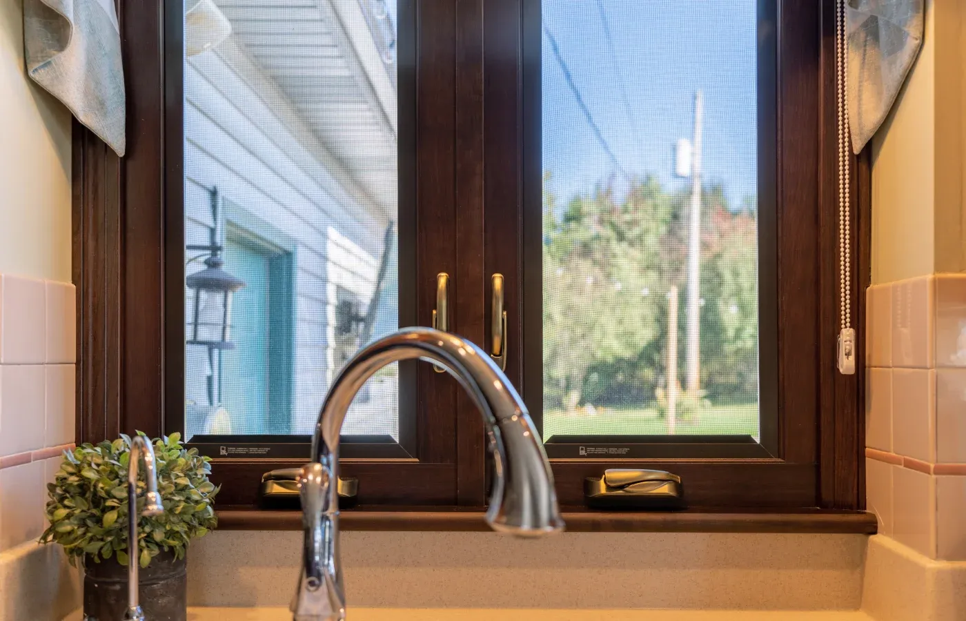 The top of a kitchen faucet with a wood-clad casement window in the background with a hazelnut finish.