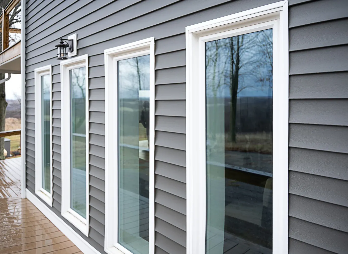 The outside of a home with new grey panel siding, white trim, and a row of four picture windows.