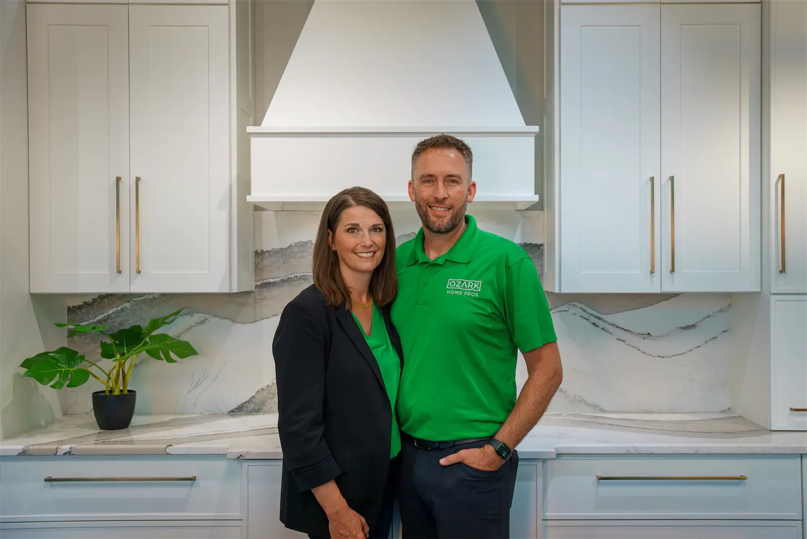 Ozark Home Pros owners stand in a kitchen with white cabinets and brass-colored fixtures.